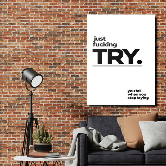 Motivační obraz na plátně „just fucking TRY“ na cihlové zdi v obýváku nad pohovkou a stojací lampou