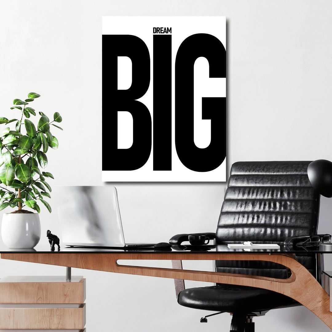 Motivační obraz na plátně s černobílým nápisem DREAM BIG pověšený v minimalistické kanceláři nad pracovním stolem