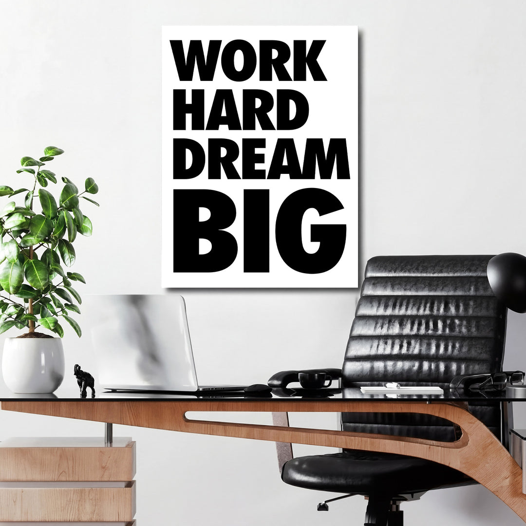 Motivační obraz na plátně WORK HARD DREAM BIG na bílé kancelářské zdi nad pracovním stolem s rostlinou a černým křeslem