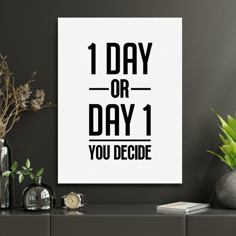 Motivační obraz na zeď s černobílým citátem „1 DAY OR DAY 1 YOU DECIDE“ v moderní kanceláři s rostlinami a hodinkami