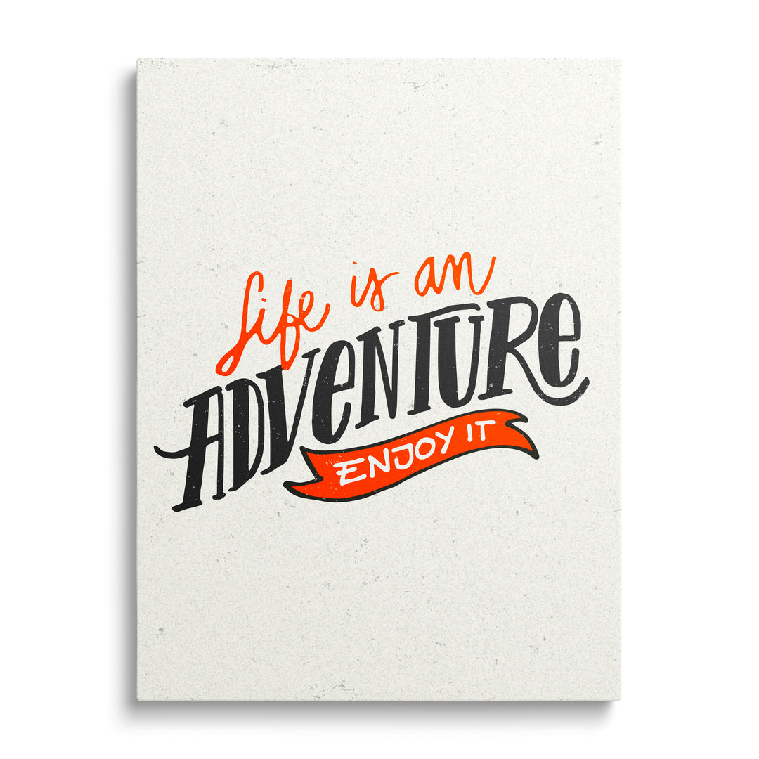 Motivační obraz na plátně s černo-oranžovým nápisem „Life is an adventure – enjoy it“, pohled zepředu