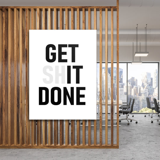 Motivační obraz na plátně s nápisem GET SHIT DONE zavěšený za dřevěnými lamelami v moderní kanceláři