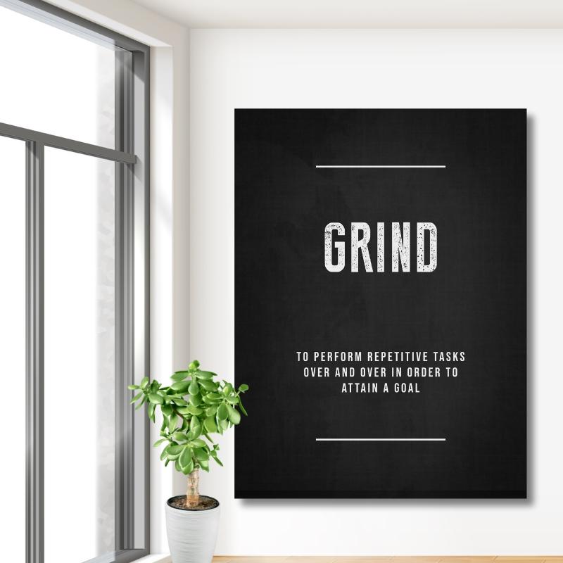 Motivační obraz na plátně s nápisem GRIND v moderní pracovně na bílé zdi u velkého okna a zelené rostliny