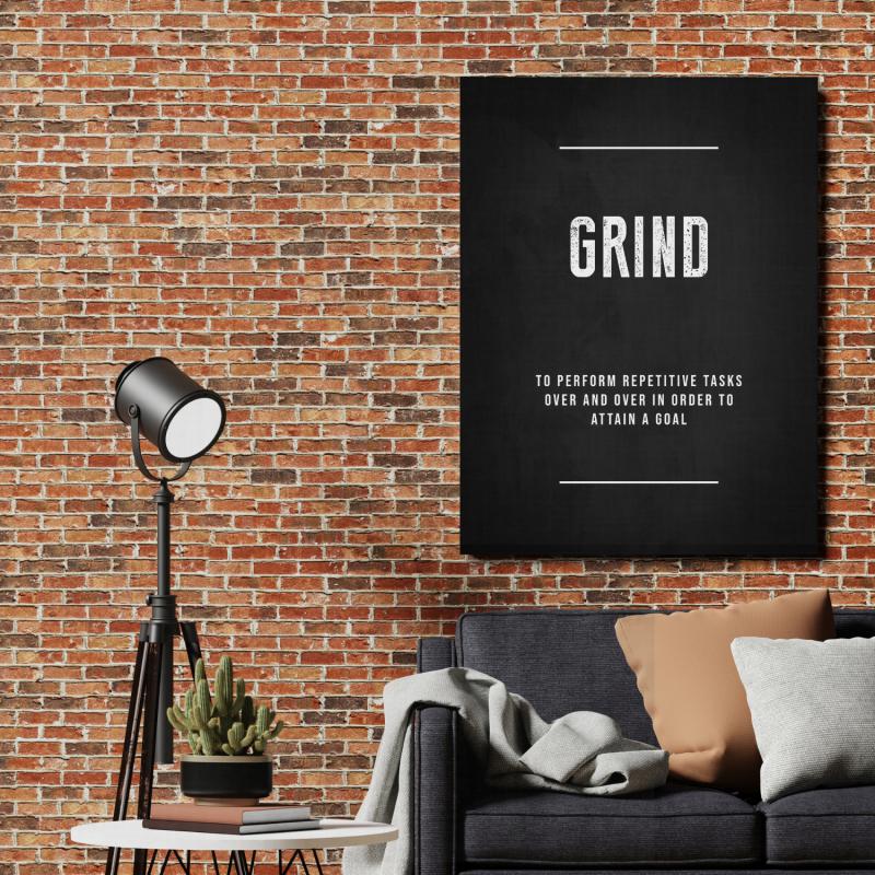 Motivační obraz na plátně s nápisem "GRIND" na cihlové zdi nad pohovkou, vedle lampy a kaktusu. BudujImperium.cz, buď motivovanej.