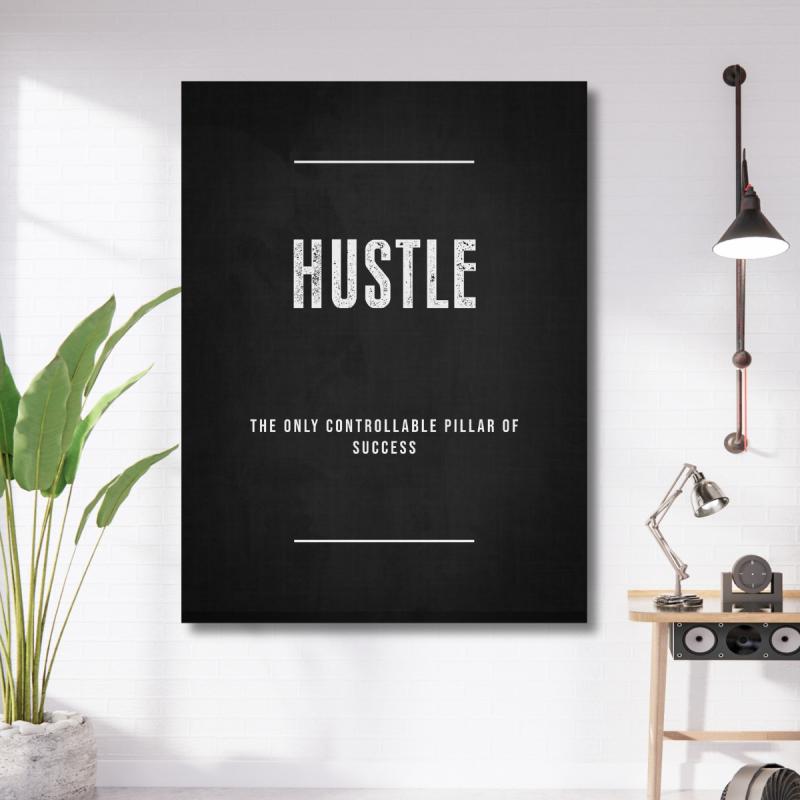 Motivační obraz na plátně s černobílým nápisem HUSTLE v minimalistické kanceláři s lampou a rostlinou