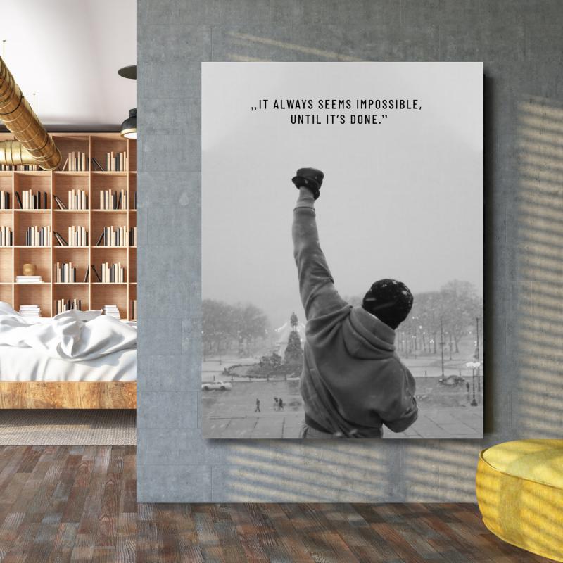 Motivační obraz na zeď s nápisem "It always seems impossible until it's done" vedle knihovny budujimperium.cz