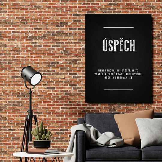 Motivační obraz na plátně s bílým nápisem „Úspěch“ nad pohovkou, stojací lampou a kaktusem na cihlové zdi